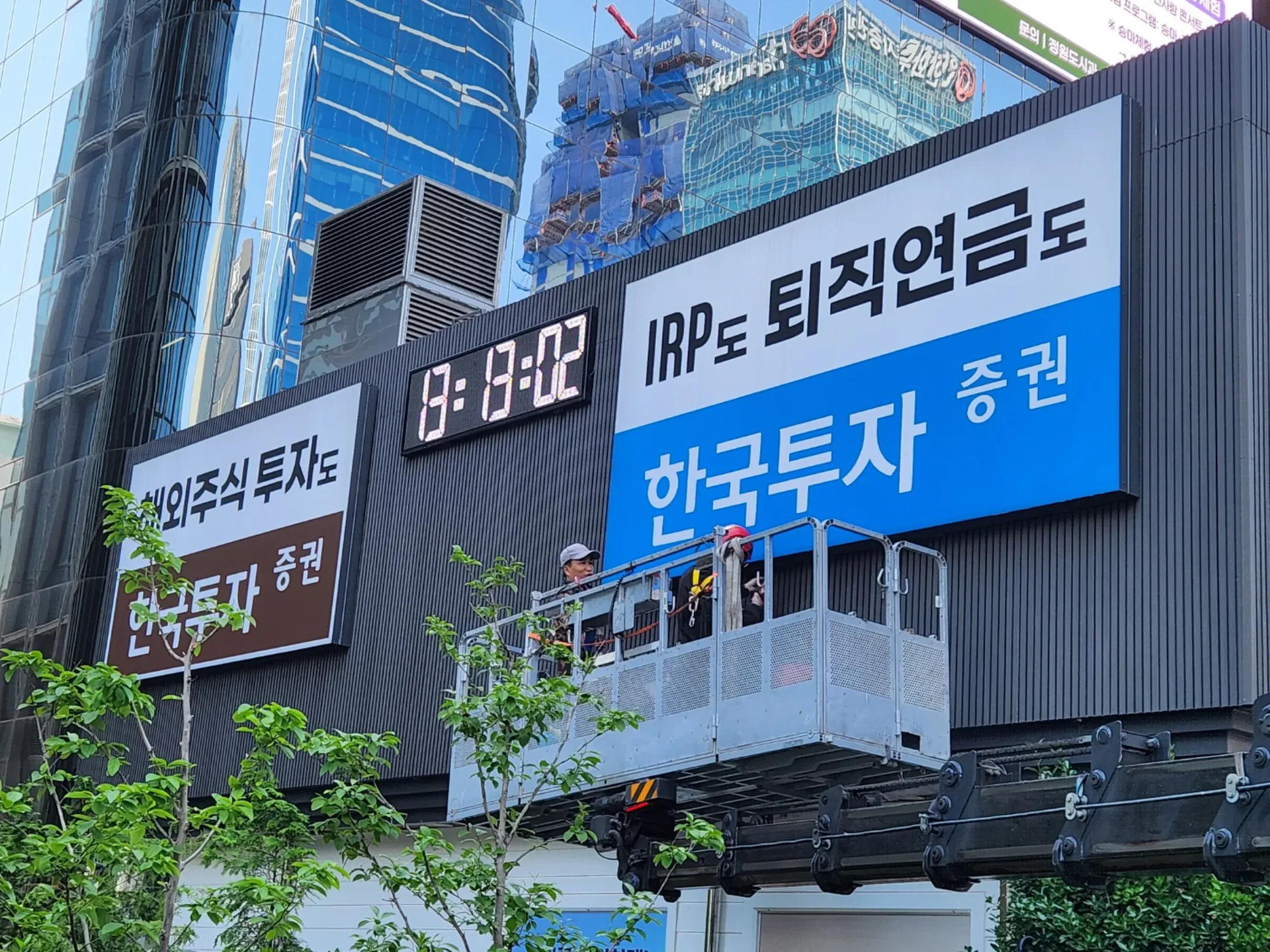 고소작업 크레인 위에서 증권사 외부간판과 디지털 시계 표시판을 점검하는 작업자들