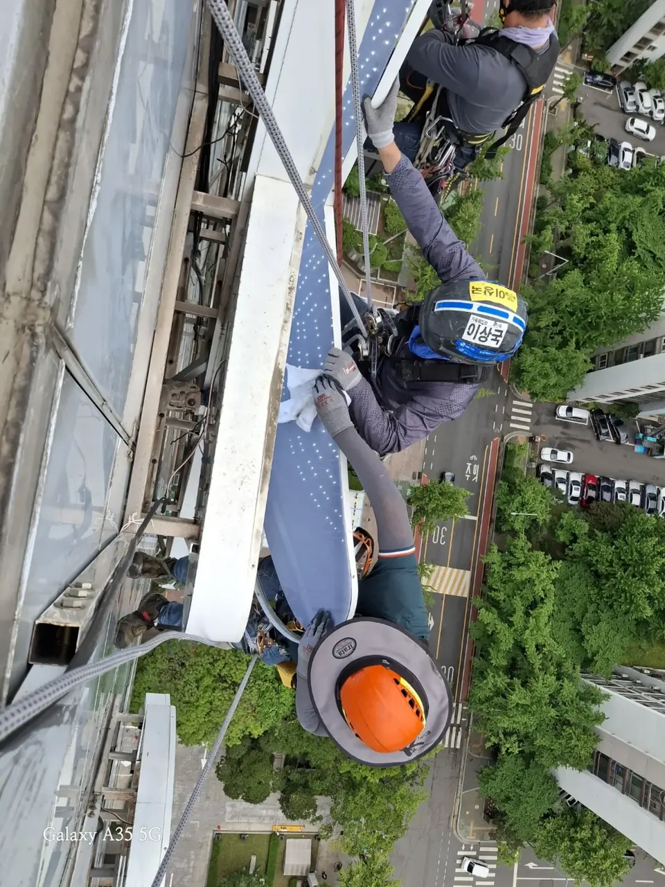 고층 건물 외벽에서 로프에 매달려 채널 간판 표면을 세척하는 작업자들